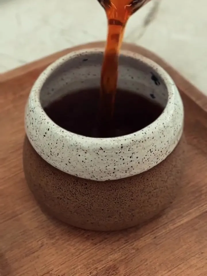 Café coado sendo servido numa xícara de cerâmica pintada, sobre uma bandeja de madeira.