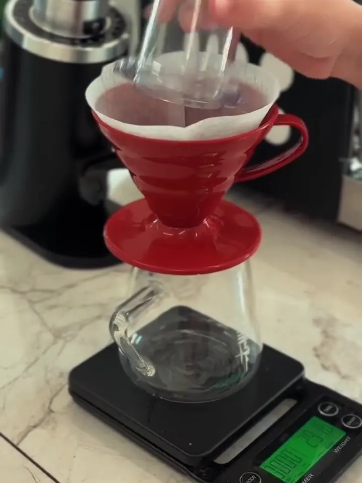 Coador V60 vermelho sobre a jarra de vidro e a balança, ao lado do moedor.