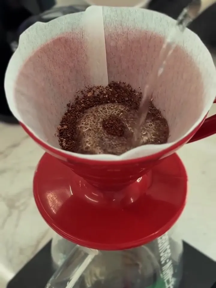 Água quente sendo despejada sobre o café moído no coador V60 vermelho.