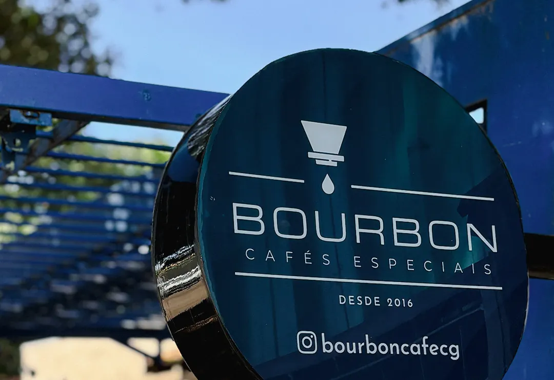 Placa circular azul do Bourbon — Cafés Especiais, desde 2016 — na entrada, sob a pérgola azul.