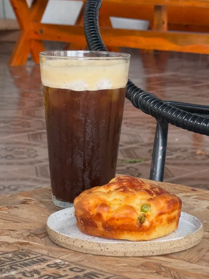 Café gelado com espuma num copo de vidro, ao lado de uma tortinha dourada.