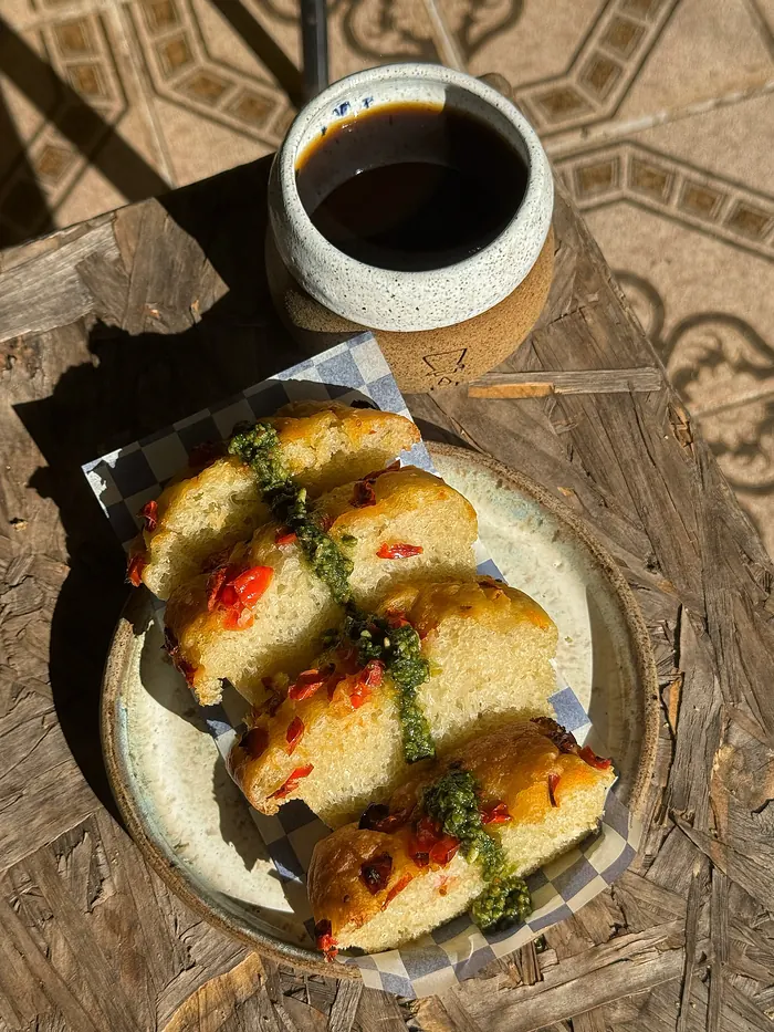Fatias de pão assado com tomate e ervas num prato de cerâmica, com uma xícara de café ao lado.