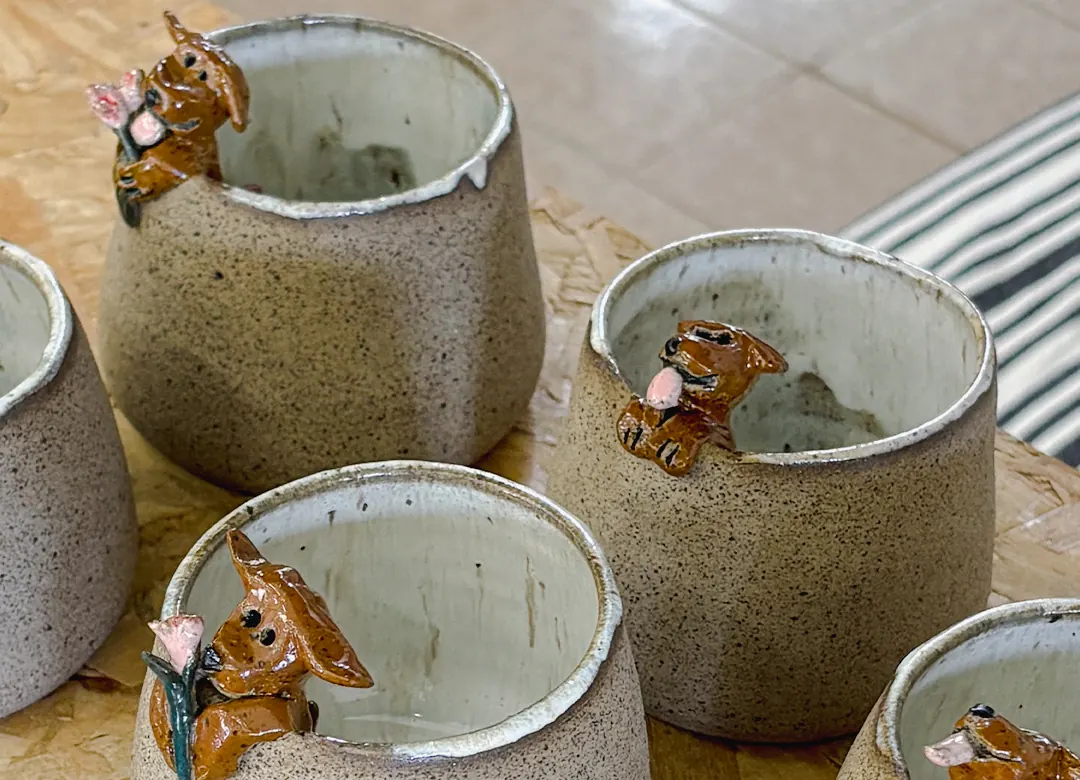 Xícaras de cerâmica artesanal com pequenos cachorros esculpidos na borda.